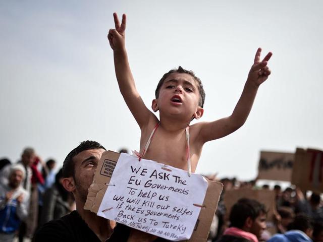 A Syrian refugee holds a child carrying a placard reading "we ask the EU governments to help us" as refugees and migrants including children who left the Chios registration camp protest on April 3, 2016 and camp out in the port of Chios. (AFP Photo) A Syrian refugee holds a child carrying a placard reading "we ask the EU governments to help us" as refugees and migrants including children who left the Chios registration camp protest on April 3, 2016 and camp out in the port of Chios. (AFP Photo)
