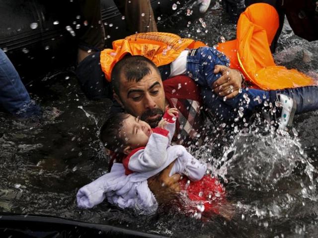 A Syrian refugee holds onto his children as he struggles to walk off a dinghy on the Greek island of Lesbos, after crossing a part of the Aegean Sea from Turkey to Lesbos September 24, 2015. (Yannis Behrakis/Reuters)