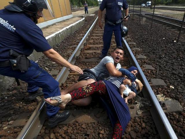 Hungarian policemen stand over a family of immigrants who threw themselves onto the track before they were detained at a railway station in the town of Bicske, Hungary, September 3, 2015. (Laszlo Balogh/REUTERS)