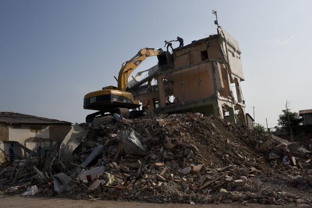 A couple of persons try to climb on the arm of a mechanical loader after attempting to recover an antenna from the roof of a destroyed building in Canoas, Ecuador. (AP Photo)