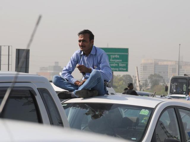 Many of Delhi’s taxis already run on CNG, but the ban will impact about 30,000 traditional cabs and some working for app-based Uber and Ola services, according to taxi operators. In this photo, a man waits on the top his car after getting caught  in a traffic jam on Delhi-Gurgaon highway. (Parveen Kumar/HT Photo) 