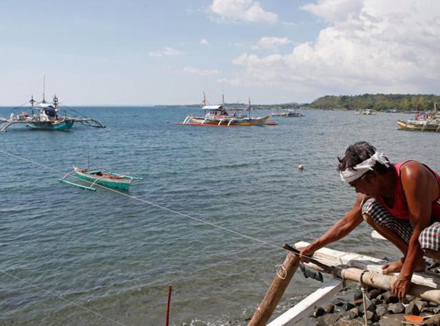 A fisherman repairs his boat overlooking fishing boats that fish in the disputed Scarborough Shoal in the South China Sea, at Masinloc, Zambales, in the Philippines April 22, 2015. (REUTERS)
