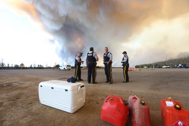 Police officers work around a road block as smoke rises from a forest fire along the highway near Fort McMurray, Alberta on Friday. (AFP) Police officers work around a road block as smoke rises from a forest fire along the highway near Fort McMurray, Alberta on Friday. (AFP)