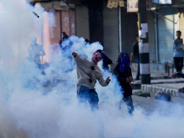 A masked protester throws back an exploded tear gas shell at Indian policemen during a protest in Srinagar on April 12.(AP)