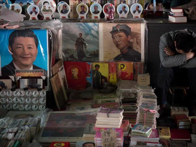 A vendor (right) takes a nap next to posters showing the late Chinese chairman Mao Zedong (centre) and Chinese President Xi Jinping (left) at a market in Beijing. Fifty years after the Cultural Revolution spread bloodshed and turmoil across China, the Communist-ruled country is driving firmly down the capitalist road but Mao Zedong's legacy remains. (AFP File Photo)