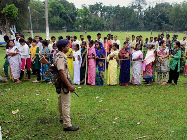 Security personnel keep vigil while people stand in a queue to cast their vote in Jorhat. (PTI Photo)