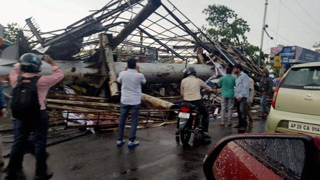 Passers-by take photographs of uprooted billboards that were dislodged due to strong winds in Hyderabad on Friday. A thunderstorm left the city in disarray. (PTI)