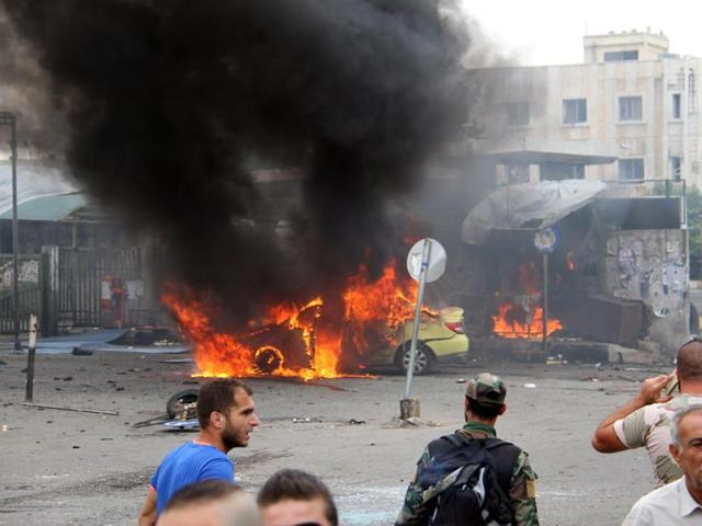 Syrians gather in front of a burning car at the scene where suicide bombers blew themselves up, in the coastal town of Tartus on Monday. (AP) Syrians gather in front of a burning car at the scene where suicide bombers blew themselves up, in the coastal town of Tartus on Monday. (AP)