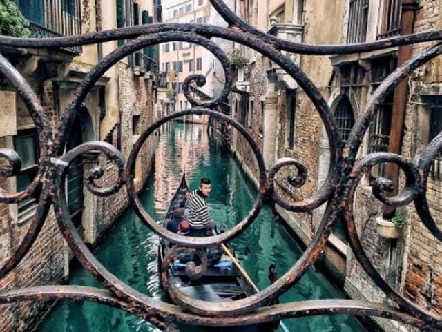 Finally, some humans. A gondolier takes his gondola through the green waters of Venice as a sly one with a camera captures him. (rastelling)