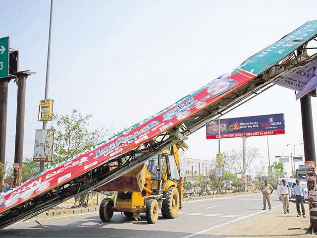 An earthmover removes the signage that came crashing on the car (above) of a retired navy personnel on NH-24 on Monday afternoon. (Sakib Ali/HT Photo) An earthmover removes the signage that came crashing on the car (above) of a retired navy personnel on NH-24 on Monday afternoon. (Sakib Ali/HT Photo)