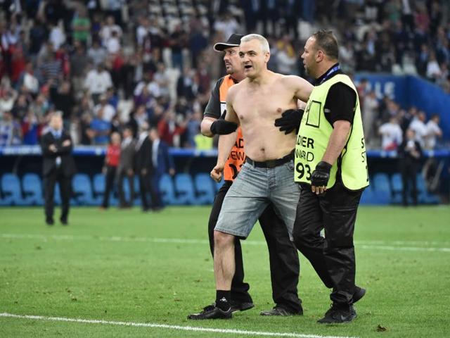 A Russia supporter is escorted off the pitch by stewards. (AFP) A Russia supporter is escorted off the pitch by stewards. (AFP)