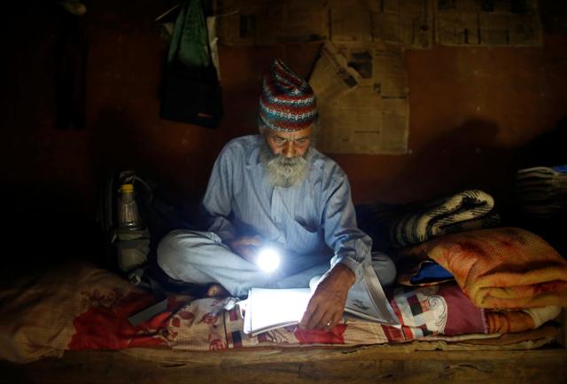 Kami uses a torch to read a book during a power cut, at his one-room house in Syangja. (REUTERS)