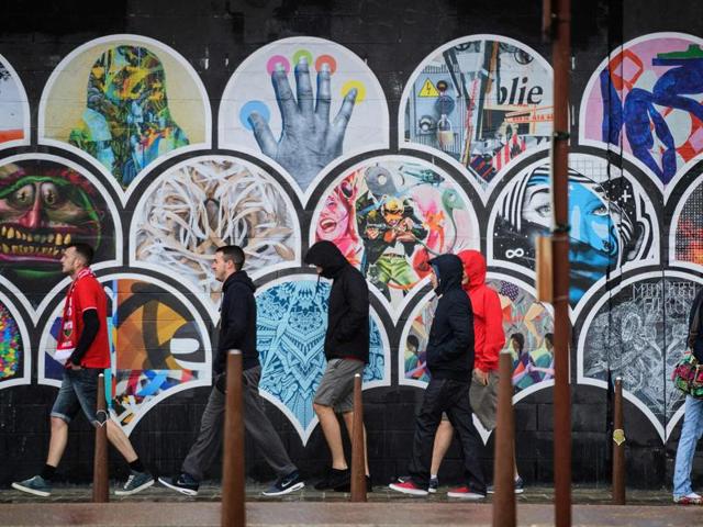 Football supporters walk past a piece of street art as they walk in heavy rain in Lens, on the day England plays against Wales in their Euro 2016 group B football match.  (AFP Photo) 