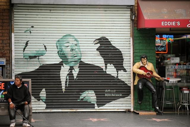 A man seated on a bench in front of a painting of director Alfred Hitchcock, and next to a statue of singer Elvis Presley on the Hollywood Walk of Fame, in Hollywood, California. (AFP)
