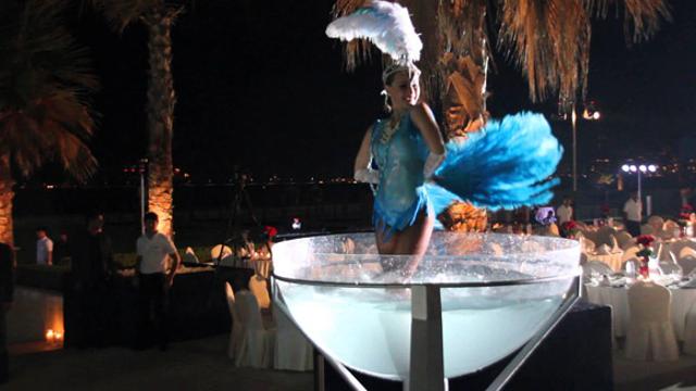 A woman dressed as a show girl stands knee deep in a large prop designed to look like a champagne glass. Foreigners are usually preferred for such stunts. A woman dressed as a show girl stands knee deep in a large prop designed to look like a champagne glass. Foreigners are usually preferred for such stunts.