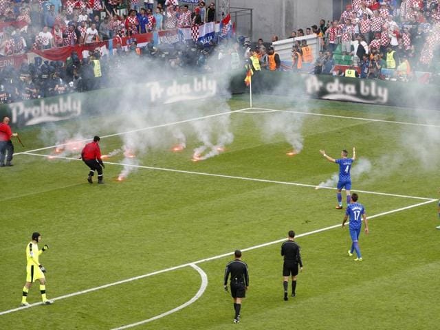 Stewards clear away flares thrown onto the pitch by fans as players look on. (REUTERS)