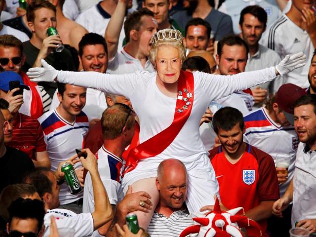An England fan wears a mask of Queen Elizabeth II as he rides on the shoulders of his mates gathering in Saint Etienne ahead of their team's match against Slovakia. (Reuters Photo)