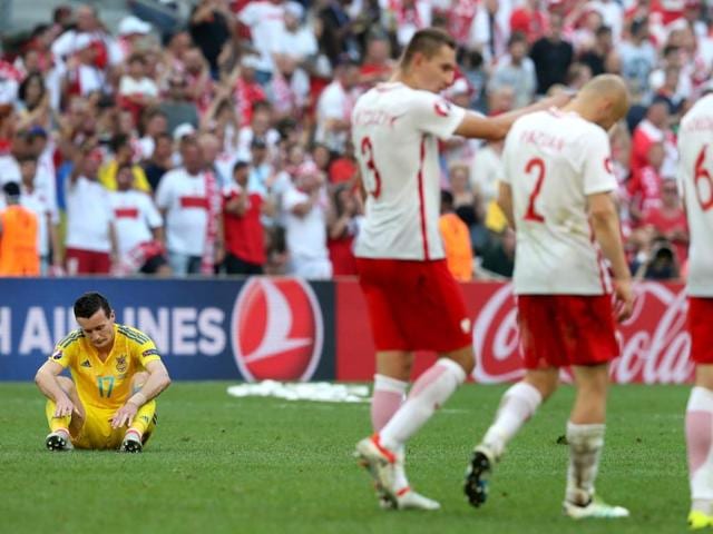 Ukraine's Artem Fedetskiy, left, sits dejected on the pitch as Polish players pass by after his team’s loss. (AP)