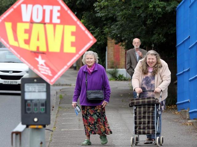 People walk past a ‘Vote Leave’ sign as they arrive to cast their ballots at a polling station in Belfast, Northern Ireland.  (AFP Photo) 