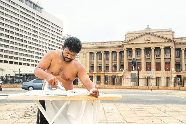 Lankan performance artist Bandu Manamperi irons his shirt in front of a government building (Photo courtesy: The artist)