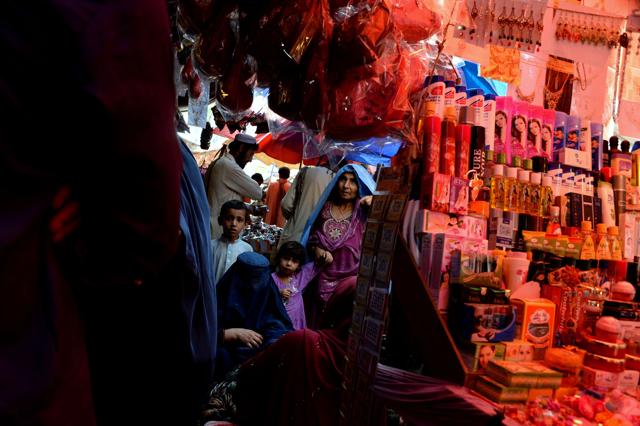 Burqa-clad Afghan women walk and children walk through a market to buy clothes for the upcoming Eid Al-Fitr festivities at a local market in Jalalabad on July 3, 2016. (AFP) 