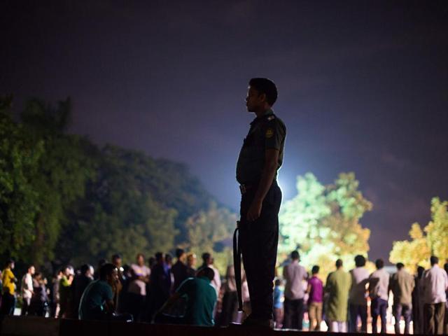 A Bangladeshi policeman keeps guard near a group of peace activists who had come together to sing and light candles in a park following an attack and seige in Dhaka . (AFP Photo) A Bangladeshi policeman keeps guard near a group of peace activists who had come together to sing and light candles in a park following an attack and seige in Dhaka . (AFP Photo)