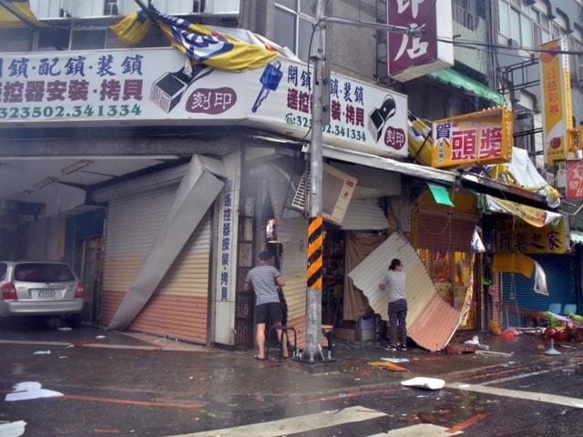 A man and a woman are seen amongst debris in front of a shop with broken shutters, towrn away by strong winds of Typhoon Nepartak in Taitung on July 8, 2016. (AFP)