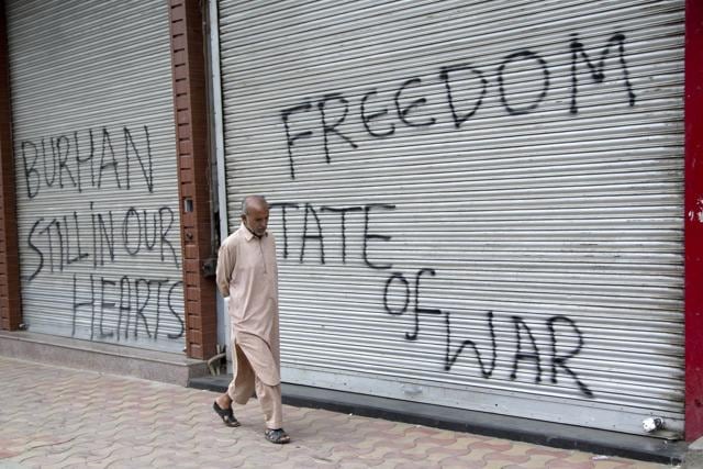 A Kashmiri man walks past closed shops painted with graffiti during a curfew in central Srinagar. (AP) A Kashmiri man walks past closed shops painted with graffiti during a curfew in central Srinagar. (AP)