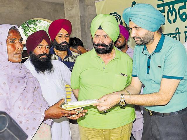 BIS Chahal (in green shirt) and his son, Bikramjit Inder Singh Chahal (right), giving away a free pair of spectacles to a woman at Kheeva Kalan in Mansa district on Sunday.(HT Photo)