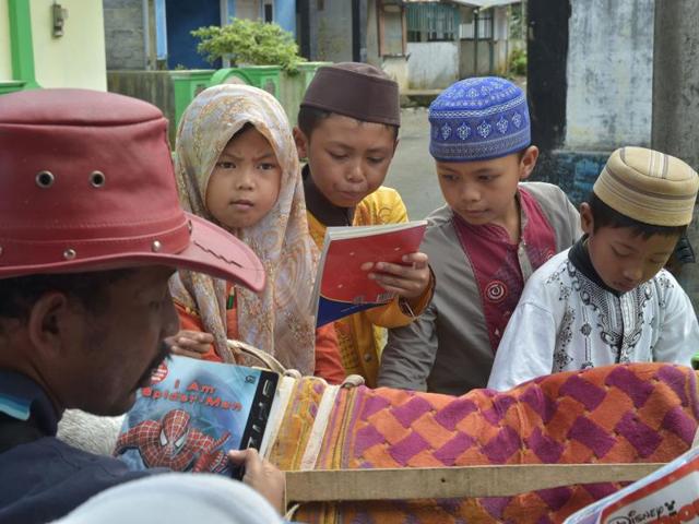 Children glance through Ridwan’s collection of books. (AFP) 