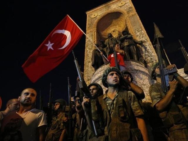Military stands guard near the the Taksim Square as people wave with Turkish flags in Istanbul. (Reuters) 