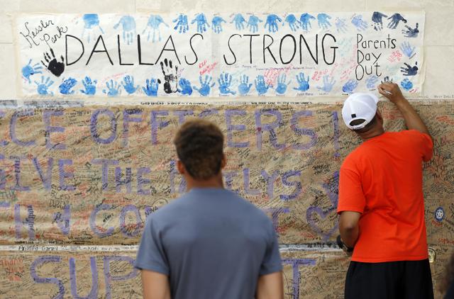 Terrell Fallon, center, watches his father Sean, of Mansfield, Texas, sign a banner attached to an exterior wall in front of the headquarters of the Dallas Police Department. (AP Photo)