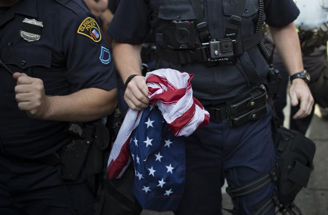 A police officer holds a US national flag that protesters attempted to burn outside the Republican National Convention in Cleveland. (AFP) A police officer holds a US national flag that protesters attempted to burn outside the Republican National Convention in Cleveland. (AFP)