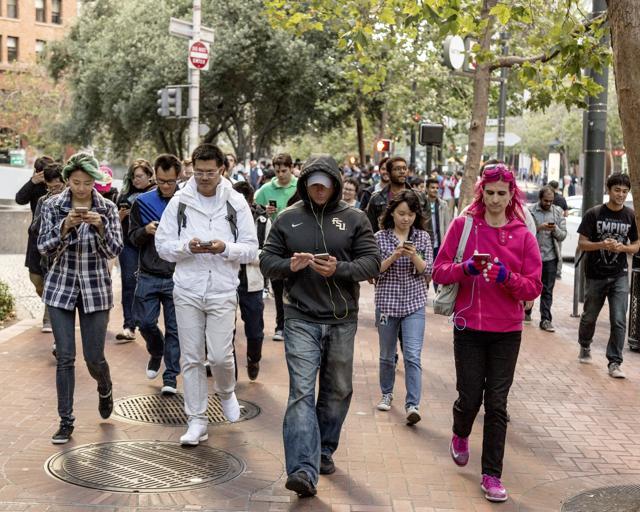 People walk up Market Street playing Pokemon Go, an augmented reality game, during a Pokemon Go Pub Crawl in San Francisco on July 20, 2016. (NYT)