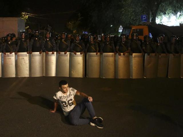 A demonstrator sits as riot police block a street near a police station, which is being occupied by an armed group, to prevent a protesters march, in Yerevan. (AP Photo) A demonstrator sits as riot police block a street near a police station, which is being occupied by an armed group, to prevent a protesters march, in Yerevan. (AP Photo)