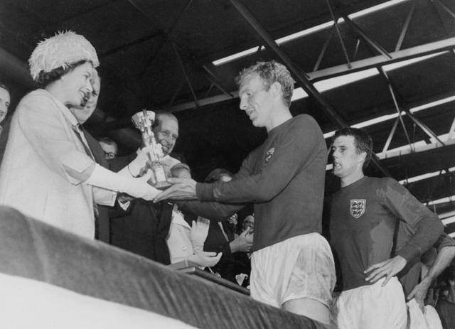 Queen Elizabeth of England presents the Jules Rimet Cup to Bobby Moore, captain of England's national soccer team, as her husband Prince Philip (C) and forward Geoff Hurst (R) look on. (AFP) Queen Elizabeth of England presents the Jules Rimet Cup to Bobby Moore, captain of England's national soccer team, as her husband Prince Philip (C) and forward Geoff Hurst (R) look on. (AFP)