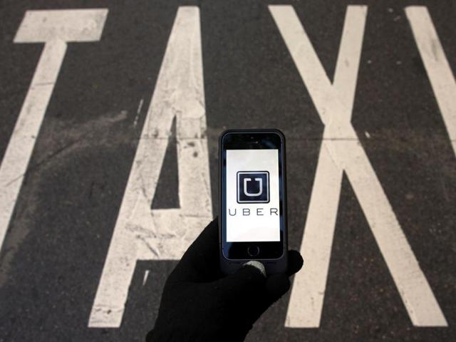 The logo of car-sharing service app Uber on a smartphone over a reserved lane for taxis in a street.(Reuters Photo)