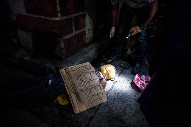 This photo taken on July 8 shows police officers investigating the body of an alleged drug dealer with his face covered with packing tape, with a cardboard sign on him reading "I'm a pusher", in a street in Manila. (AFP) This photo taken on July 8 shows police officers investigating the body of an alleged drug dealer with his face covered with packing tape, with a cardboard sign on him reading "I'm a pusher", in a street in Manila. (AFP)
