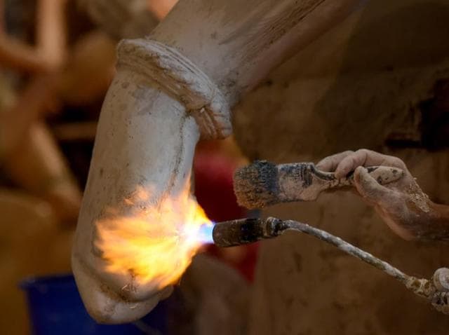 Fire for Festivities: A sculptor uses a flame torch and a brush for an idol at a city workshop on Tuesday.  (Pratik Chorge) 