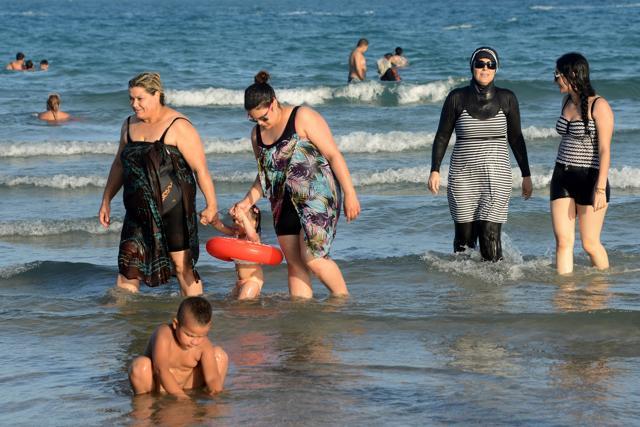 Tunisian women, one wearing a burkini, a full-body swimsuit designed for Muslim women, walk in the water at Ghar El Melh beach near Bizerte, northeast of the capital Tunis. (AFP) Tunisian women, one wearing a burkini, a full-body swimsuit designed for Muslim women, walk in the water at Ghar El Melh beach near Bizerte, northeast of the capital Tunis. (AFP)
