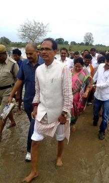 A security officer carries Madhya Pradesh chief minister Shivraj Singh Choiuhan's shoes as he walks barefoot during a survey of the flood-hit Panna district. (HT Photo) A security officer carries Madhya Pradesh chief minister Shivraj Singh Choiuhan's shoes as he walks barefoot during a survey of the flood-hit Panna district. (HT Photo)