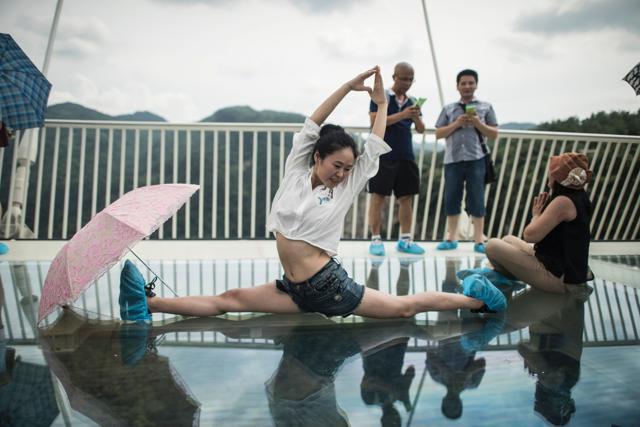 A woman does a split on the world's highest and longest glass-bottomed bridge in Zhangjiajie. Visitors were required to wear protective footwear on the opening day of the bridge on August 20. (AFP) A woman does a split on the world's highest and longest glass-bottomed bridge in Zhangjiajie. Visitors were required to wear protective footwear on the opening day of the bridge on August 20. (AFP)