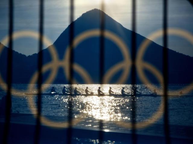 Rowers are seen through a screen decorated with the Olympic rings as they practice at the rowing venue in Lagoa at the 2016 Summer Olympics in Rio de Janeiro on August 7, 2016. (David Goldman/ AP Photo) 