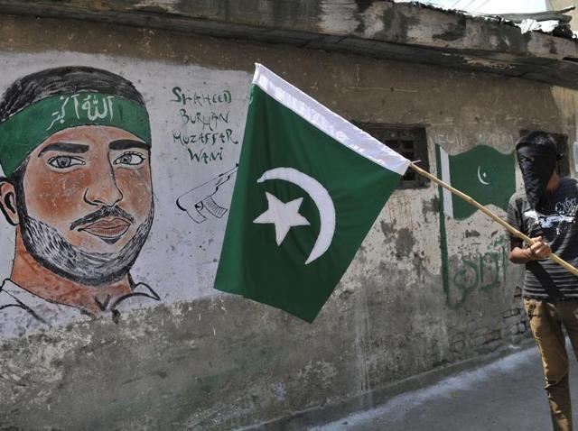 A masked Kashmiri protester holds a flag of Pakistan near a graffiti of a Hizbul Mujahideen commander Burhan Muzaffar Wani in Srinagar.(Waseem Andrabi/HT File Photo)