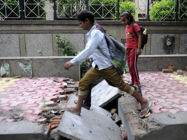 Children cross a broken pavement in the sector, which residents said is due to poor maintenance and frequent restructuring of the area for Noida Authority’s projects. (Sunil Ghosh/HT Photo) Children cross a broken pavement in the sector, which residents said is due to poor maintenance and frequent restructuring of the area for Noida Authority’s projects. (Sunil Ghosh/HT Photo)