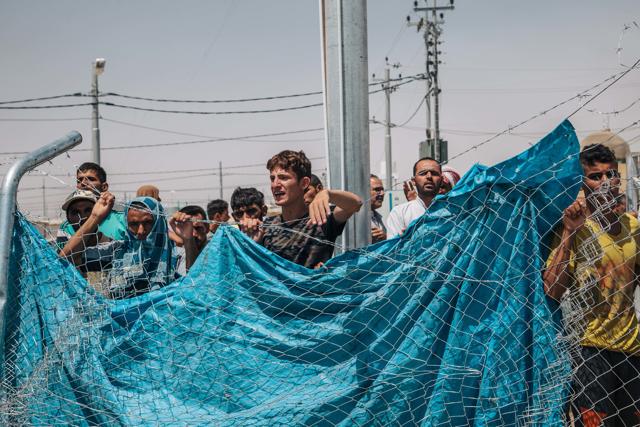 In this August 17, 2016 photo, men wait outside a fenced area at the Dibaga Camp for displaced people, where newcomers are interrogated before being allowed to stay, in Hajj Ali, northern Iraq. (AP)