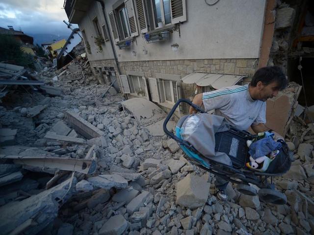 A man carries a pram among damaged buildings after a strong earthquake hit Amatrice. (AFP Photo)