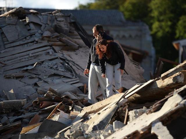 Residents stand among damaged buildings after a strong earthquake hit Amatrice. (AFP Photo)