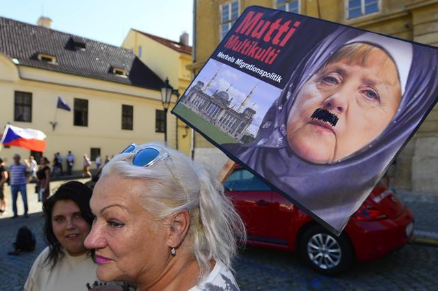 A woman holds a banner with caricature of German Chancellor Angela Merkel during a rally in Prague. (AP Photo)