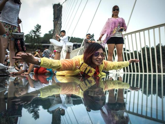 A visitor poses for a photograph on the world's highest and longest glass-bottomed bridge above a valley in Zhangjiajie. (AFP) 